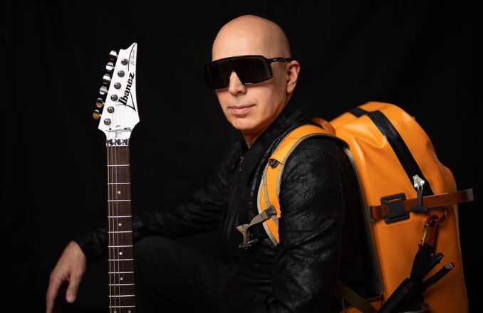 Joe Satriani photo with guitar and backpack.