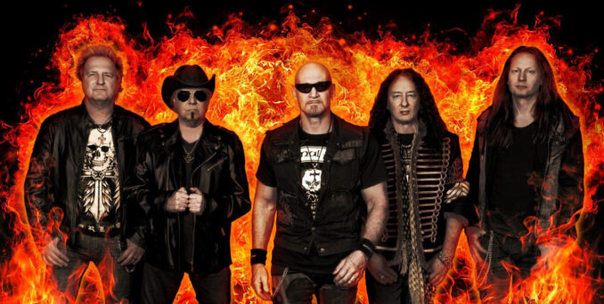 primal Fear band members standing before a wall of flames.